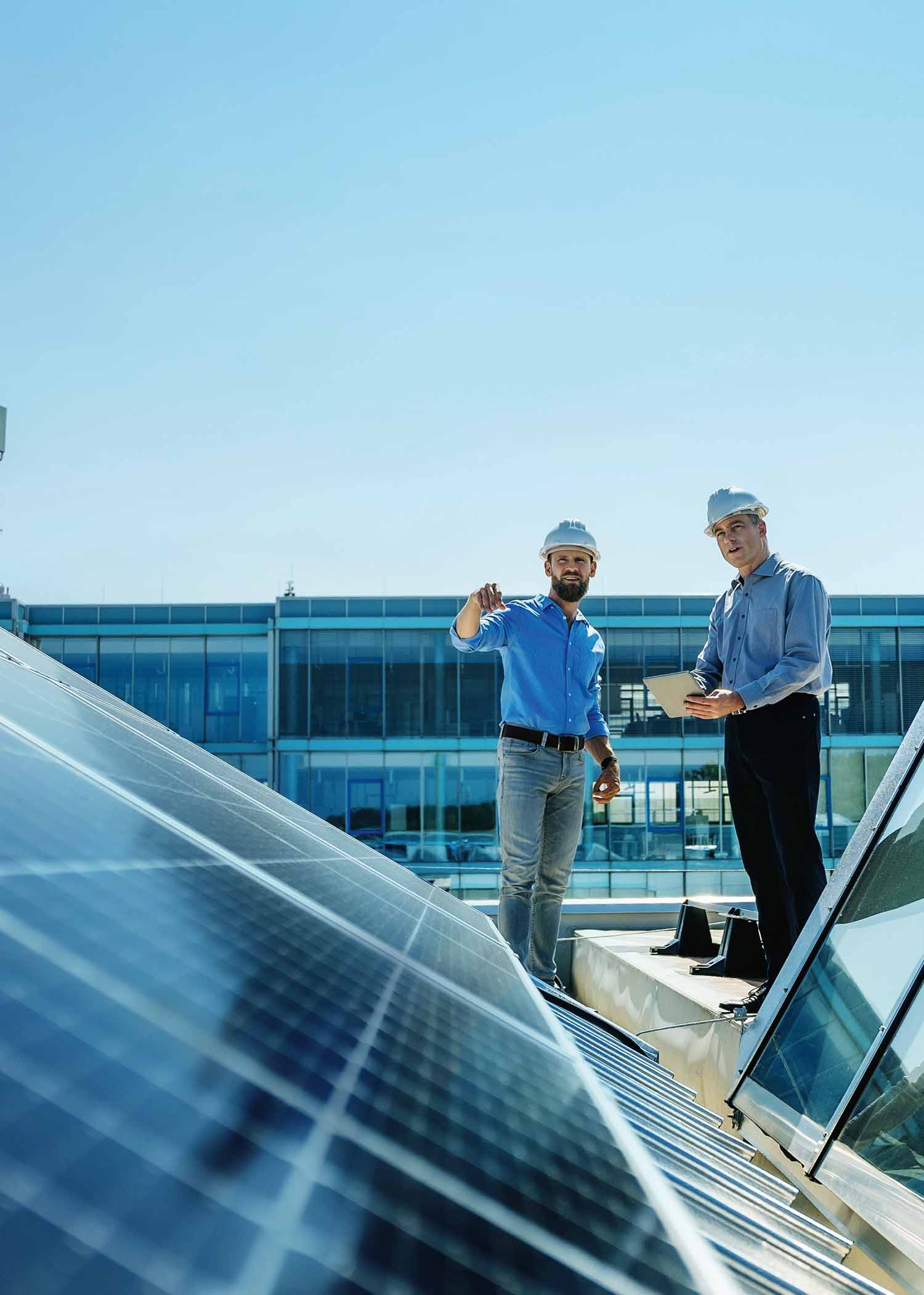 Handwerker auf einem Dach betrachten eine Photovoltaikanlage