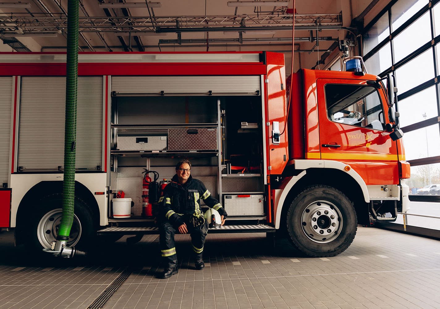 Feuerwehrmann sitzt lachend auf dem Feuerwehrauto in einer Feuerwache.
