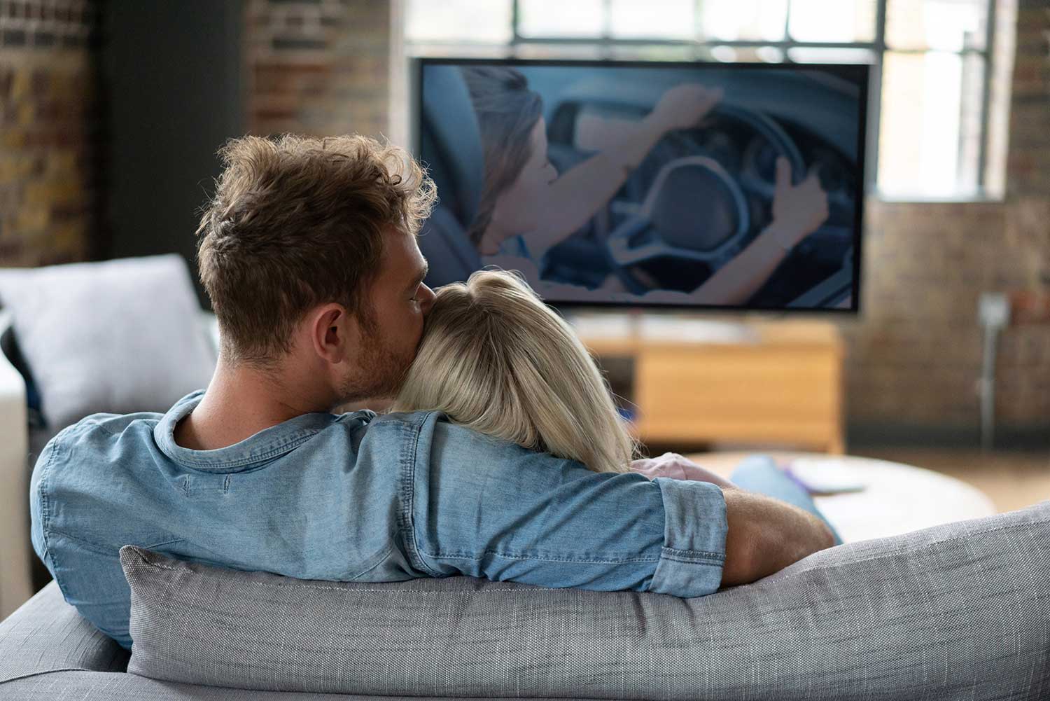 Paar sitzt kuschelnd auf der Couch und schaut TV