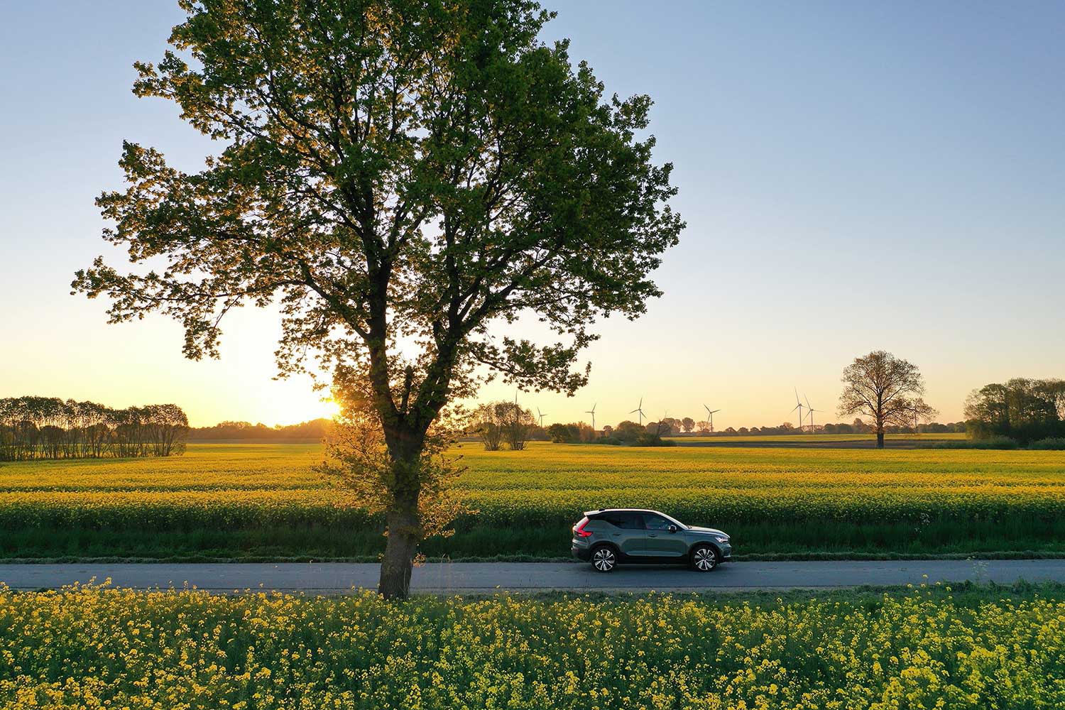 Elektroauto fährt in der Natur mit Windrädern im Hintergrund