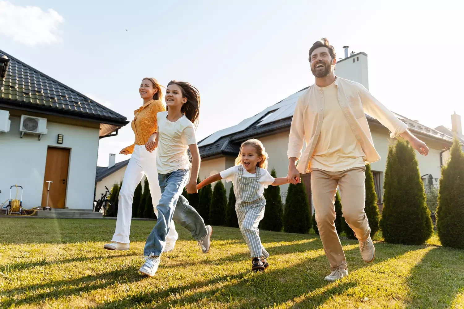 Glückliche Familie, die im Garten ihres Hauses mit Photovoltaik läuft.