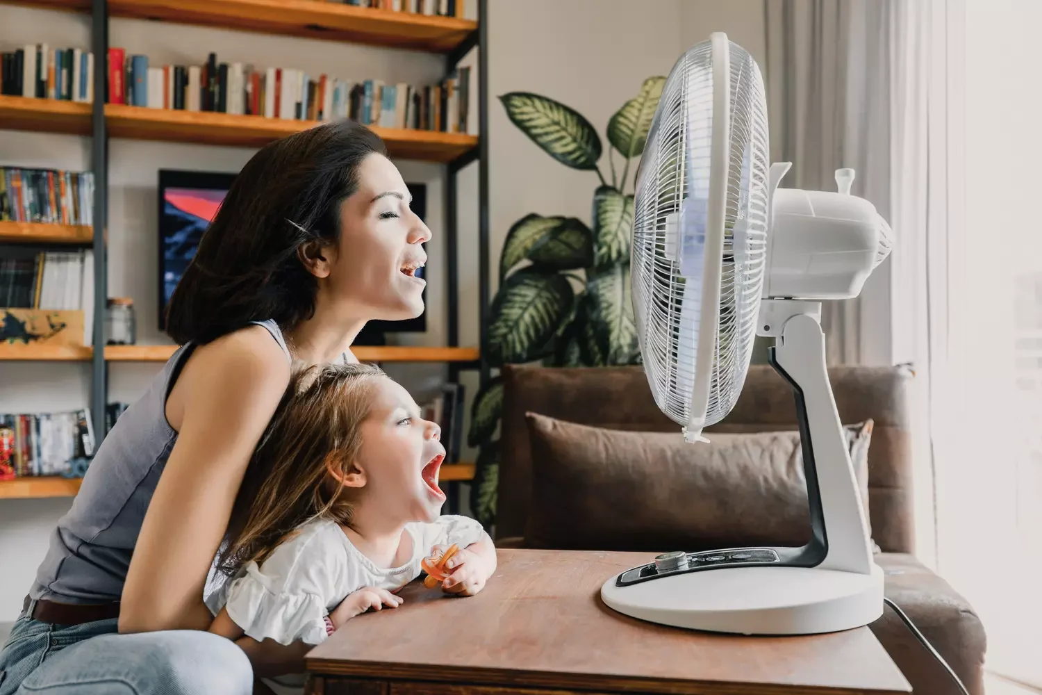 Titelbild Mutter und Tochter erfrischen sich zu Hause vor elektrischem Ventilator.