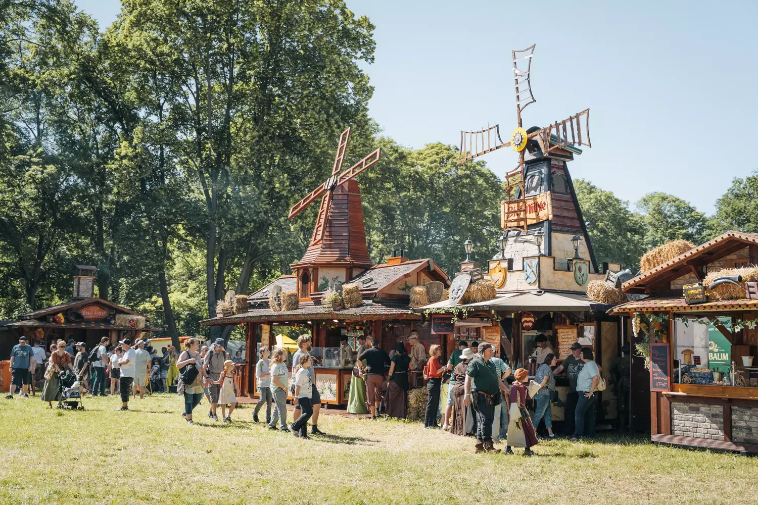 Mittelalter-Markt im Freien mit Holzbuden, Zelten und Personen in Gewandung.