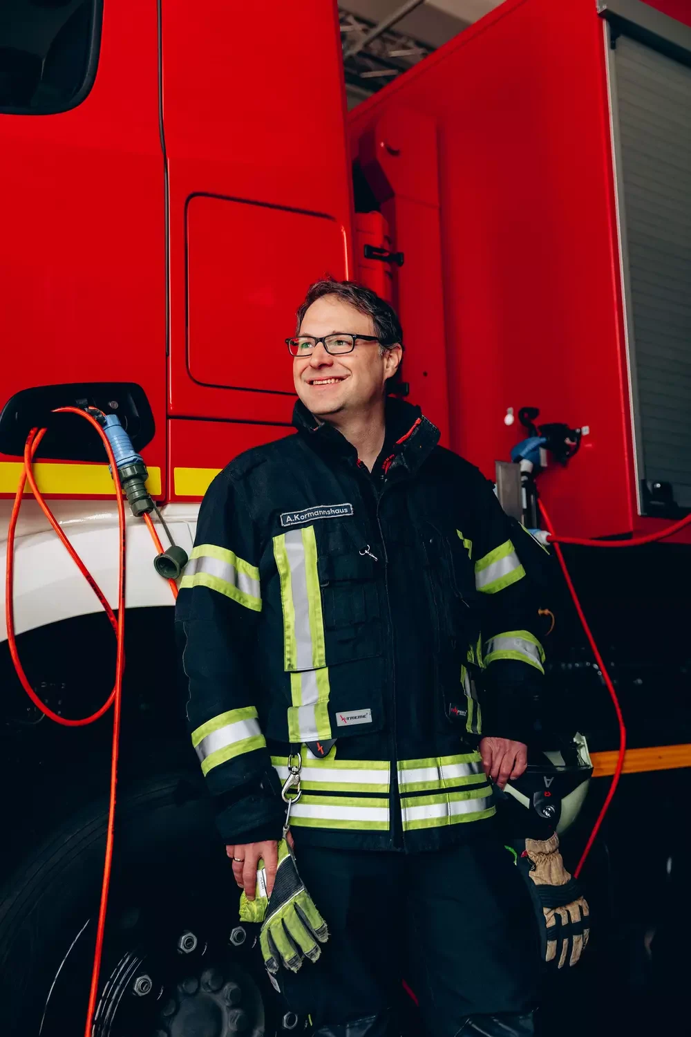Feuerwehrmann steht lachend vor Feuerwehrauto.