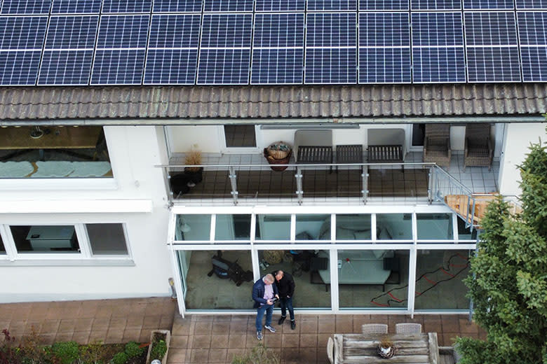 Zwei Männer stehen vor einem Haus mit einer Photovoltaikanlage auf dem Dach Zwei Männer stehen vor einem Haus mit einer Photovoltaikanlage auf dem Dach