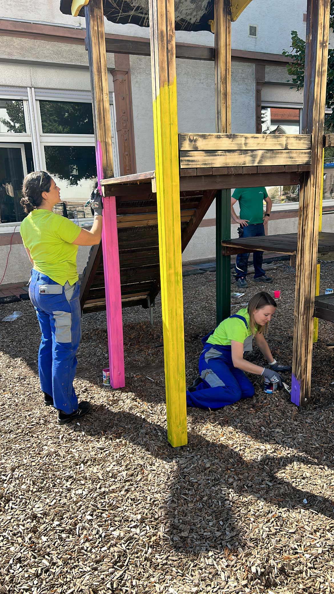 Zwei EWR Mitarbeiterinnen streichen ein Klettergerüst der Kita St. Peter