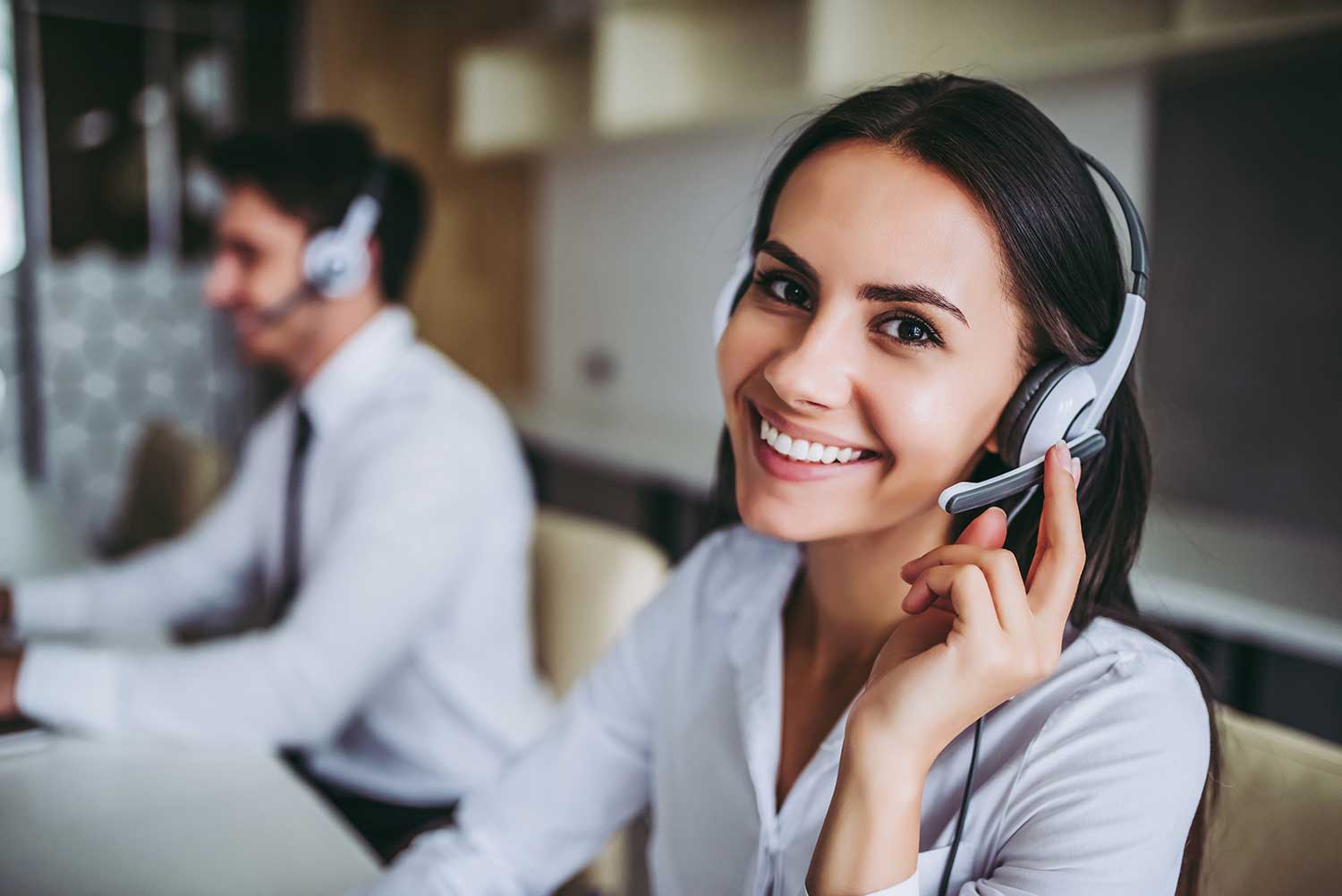Lächelnde Call Center-Mitarbeiterin mit Kollegen im Hintergrund