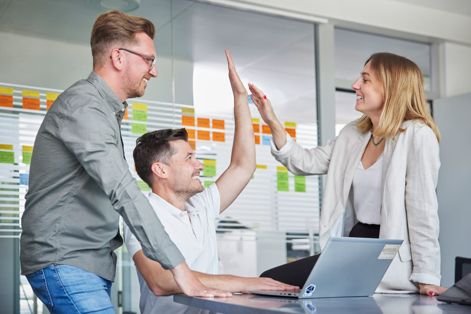 Drei Mitarbeiter im Büro, zwei geben sich ein high five