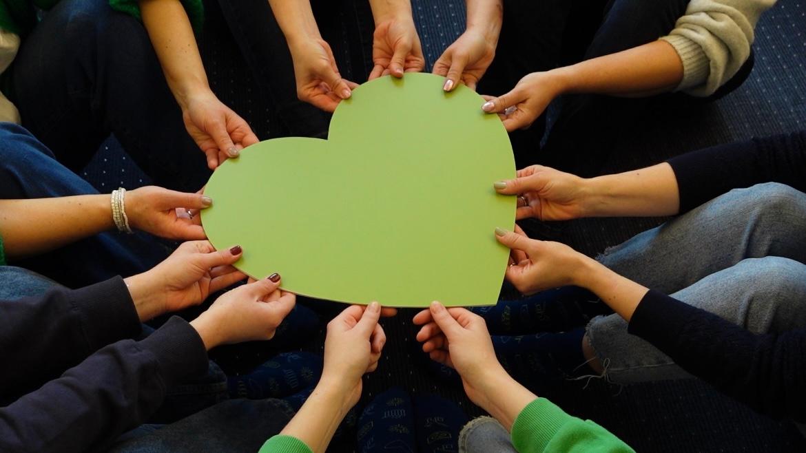 Viele Hände halten ein grünes Herz