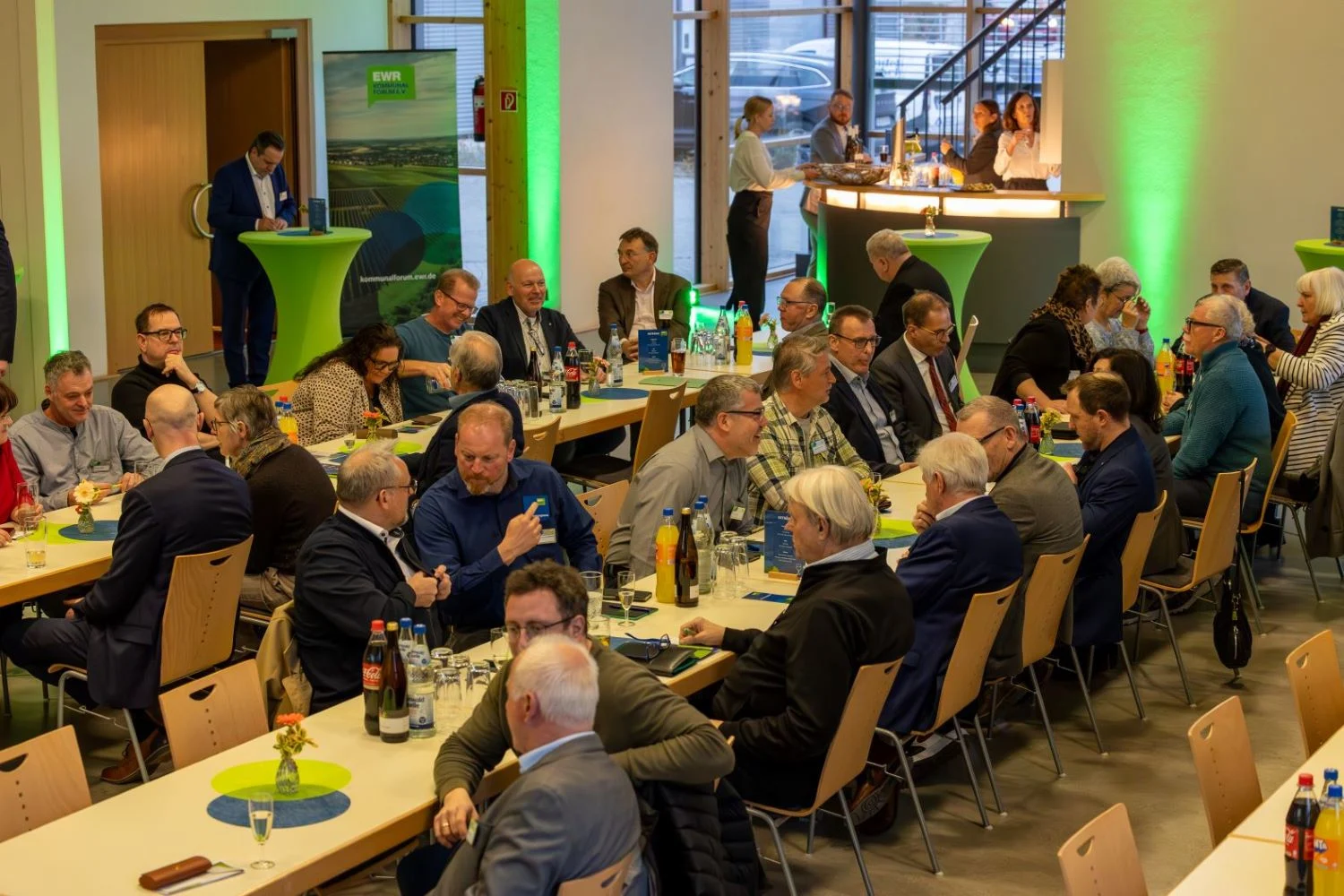 In einem großen Saal sitzen Personen an Tischen und unterhalten sich