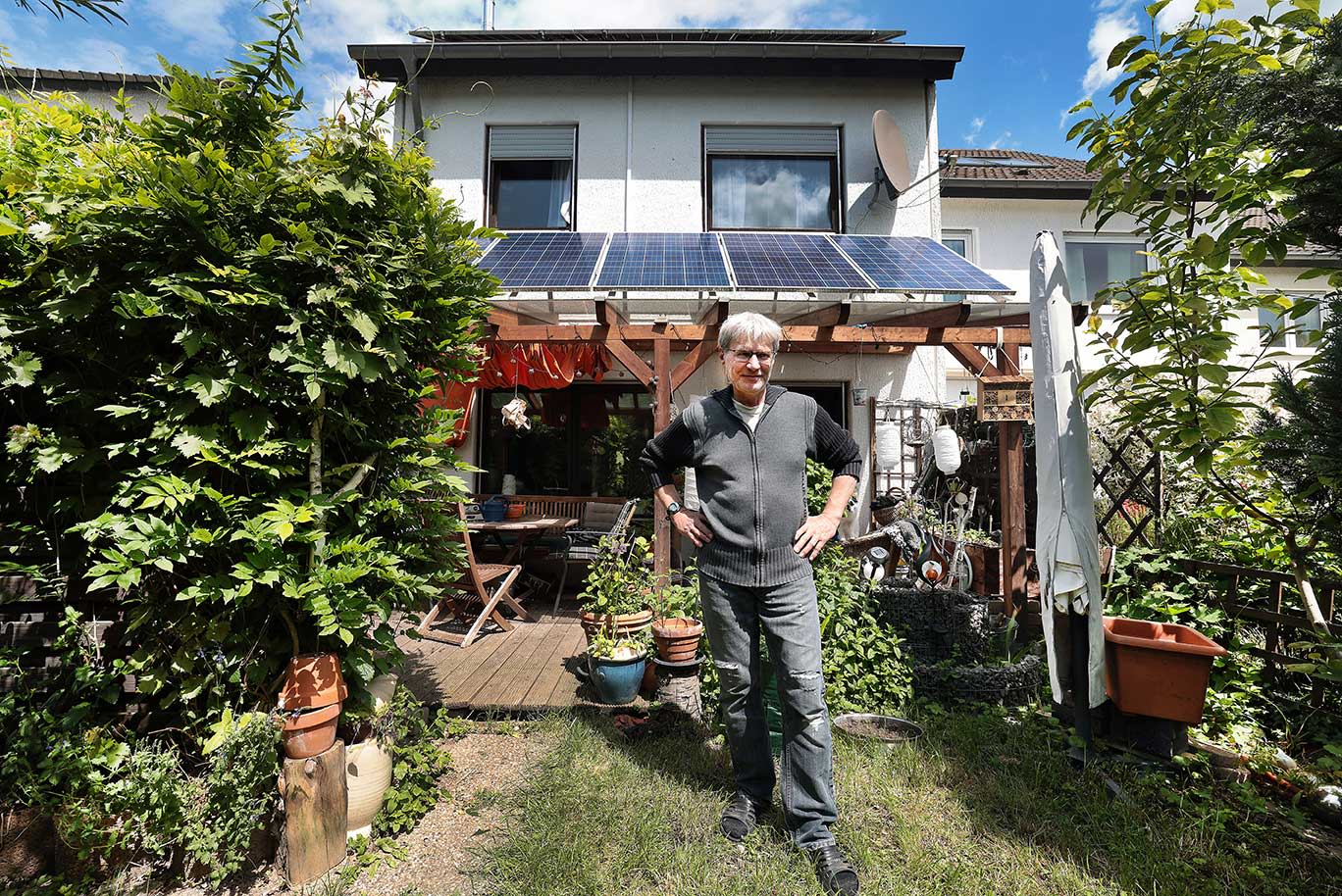 Titelbild Ein Mann steht im Garten eines Hauses mit einer Photovoltaikanlage