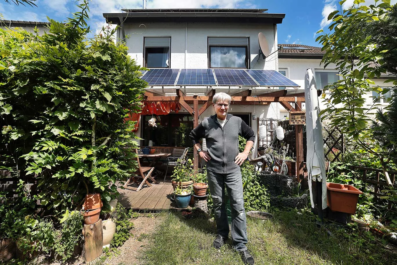 Titelbild Ein Mann steht im Garten eines Hauses mit einer Photovoltaikanlage
