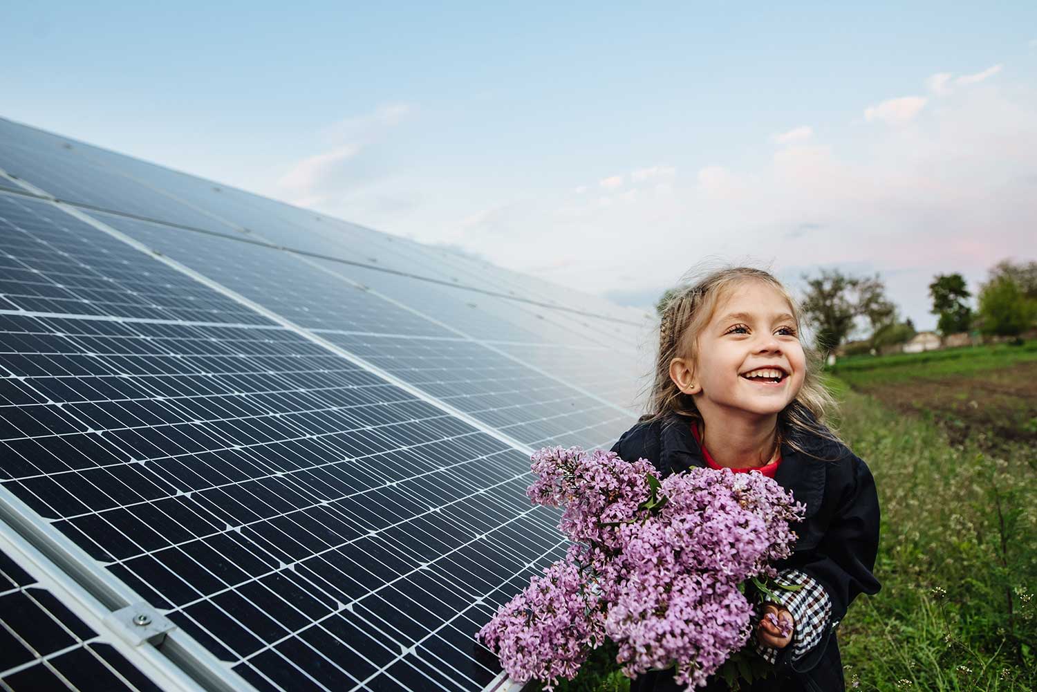 Ein Mädchen hält Blumen vor einer Photovoltaikanlage