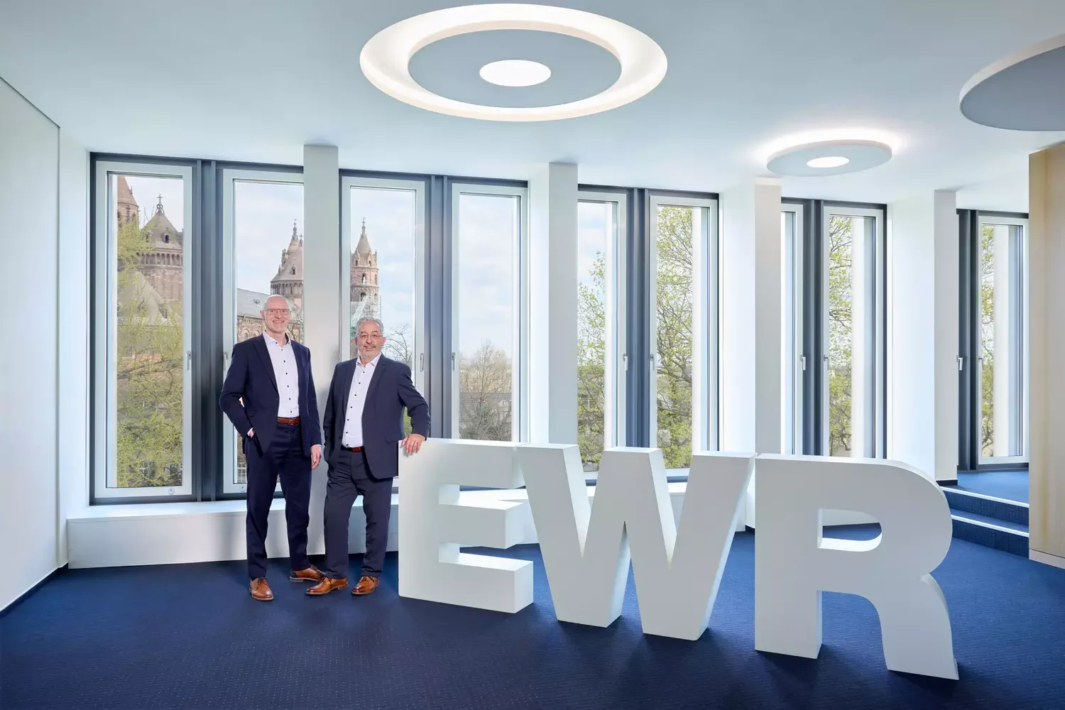 Gruppenfoto von zwei männlichen Personen im Anzug neben einem großen Schriftzug mit drei Buchstaben EWR im Hintergrund der Wormser Dom: Vorstand der EWR AG Stephan Wilhelm und Dieter Lagois