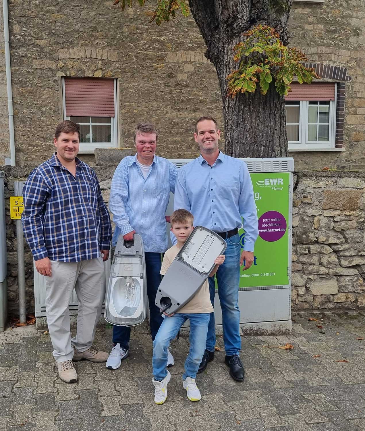 Ortsbürgermeister Daniel Kölsch hält symbolisch eine alte Leuchte in der Hand und der zehnjährige Mattis Ferber zeigt stolz eine moderne LED-Leuchte.