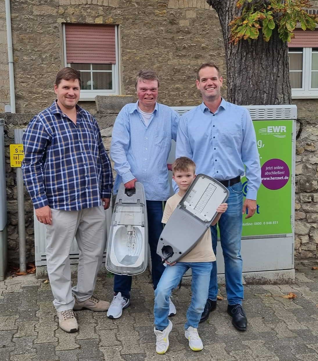 Titelbild Ortsbürgermeister Daniel Kölsch hält symbolisch eine alte Leuchte in der Hand und der zehnjährige Mattis Ferber zeigt stolz eine moderne LED-Leuchte.