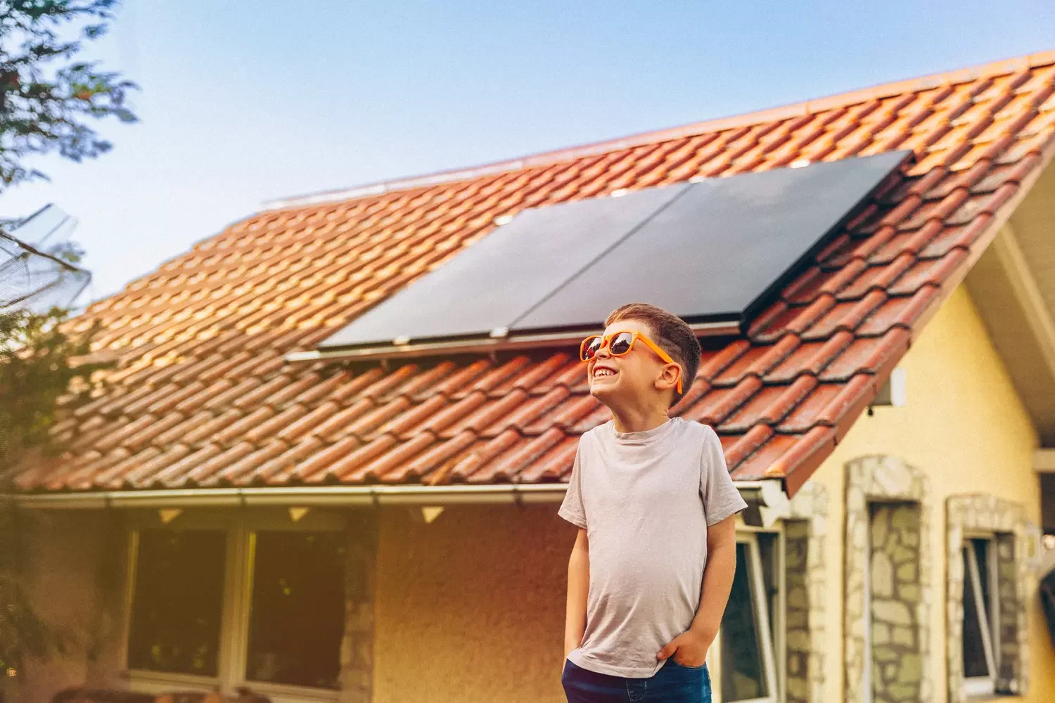 Ein Junge mit Sonnenbrille steht vor einem Haus mit Photvoltaikmodul auf dem Dach