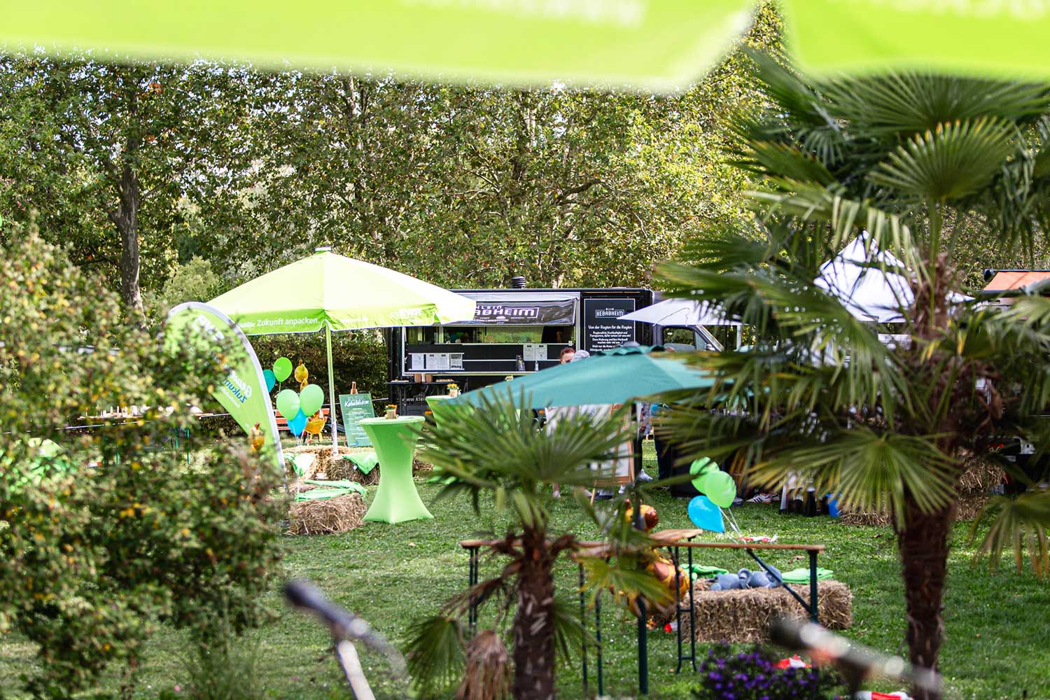 Grüne EWR-Schirme, Stehtische und Beachflags in einem Garten