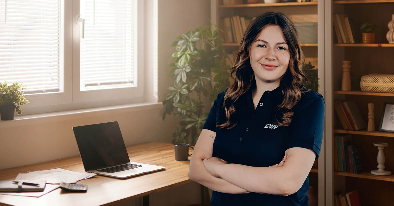 Dana steht in einem Zimmer mit Schreibtisch und Laptop im Hintergrund.