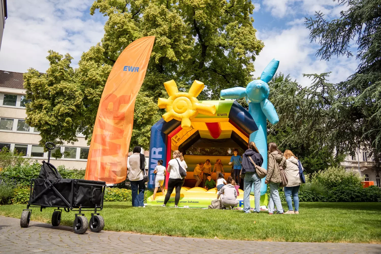 EWR Hüpfburg auf einer Wiese. Personen stehen vor der Hüpfburg und beobachten ihre Kinder beim hüpfen.