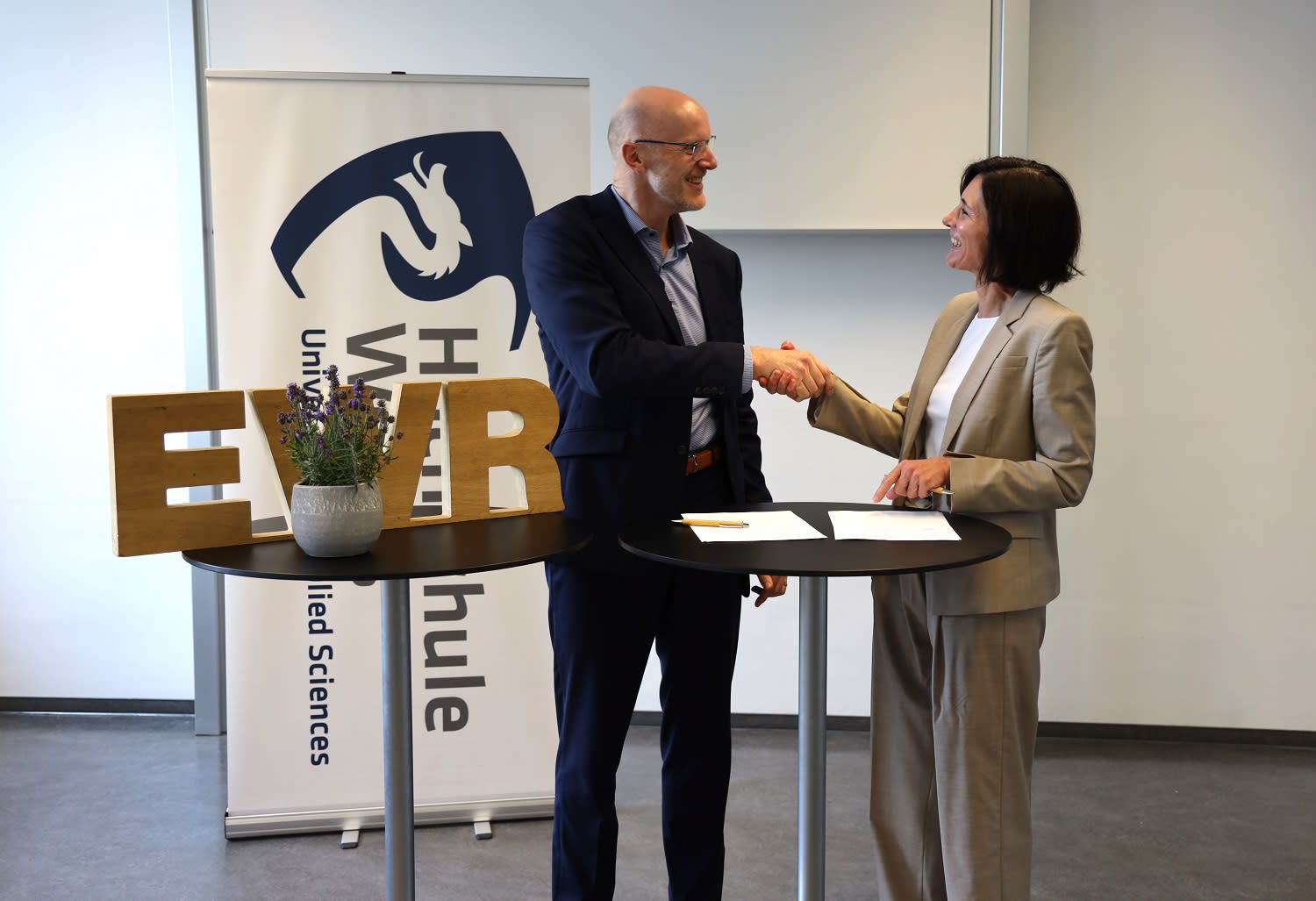 Titelbild Dieter Lagois schüttelt Frau Prof. Dr. Alexandra Nonnenmacher die Hand. Auf einem Hochtisch liegt ein Vertrag.