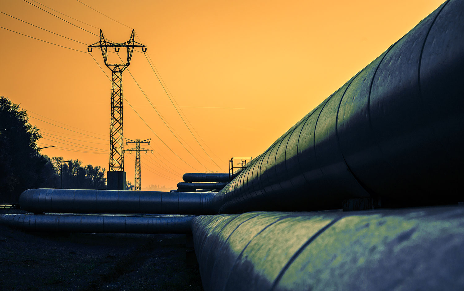 Strommaste und Fernwärmerohre bei Sonnenaufgang.