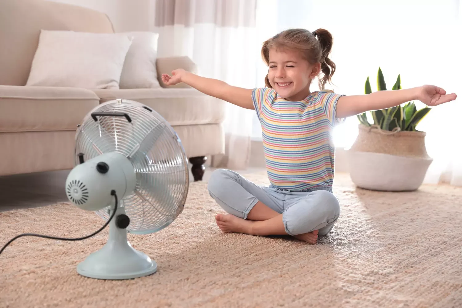Kleines Mädchen, das den Luftstrom vom Ventilator auf dem Boden im Wohnzimmer genießt