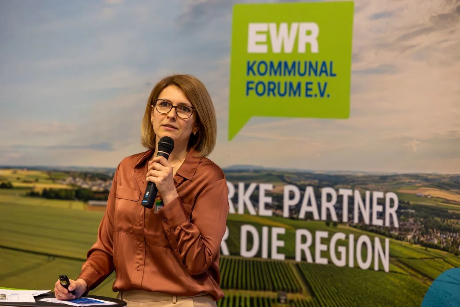 Julia Antipca, Mitarbeiterin der EWR AG, steht vor der Fotoleinwand des EWR-Kommunalforums und spricht in ein Mikrofon