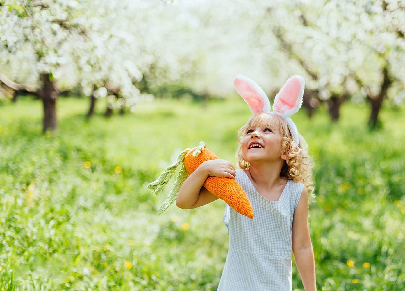 Fröhliches Mädchen mit Karotte und Hasenohren im Garten Fröhliches Mädchen mit Karotte und Hasenohren im Garten