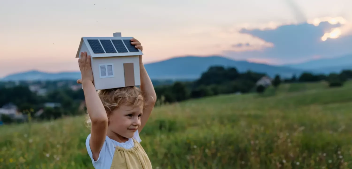 ein Mädchen hält ein Haus mit einer PV-Anlage über den Kopf