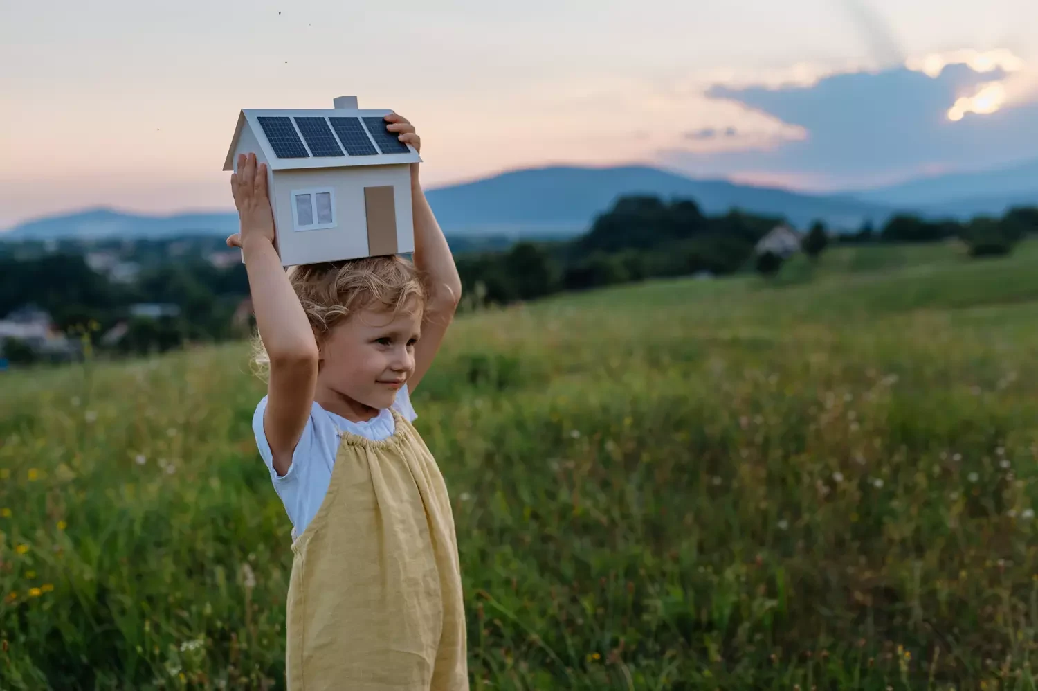 ein Mädchen hält ein Haus mit einer PV-Anlage über den Kopf