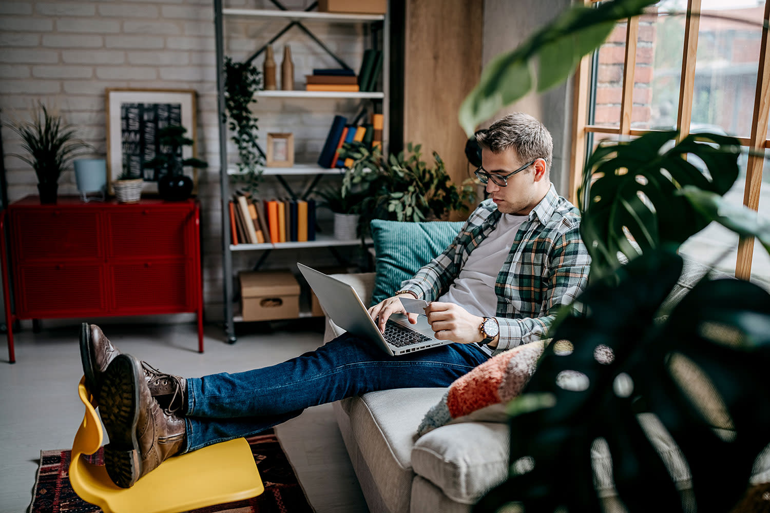 Junger Mann sitzt am Laptop auf der Couch in einer modernen Wohnung
