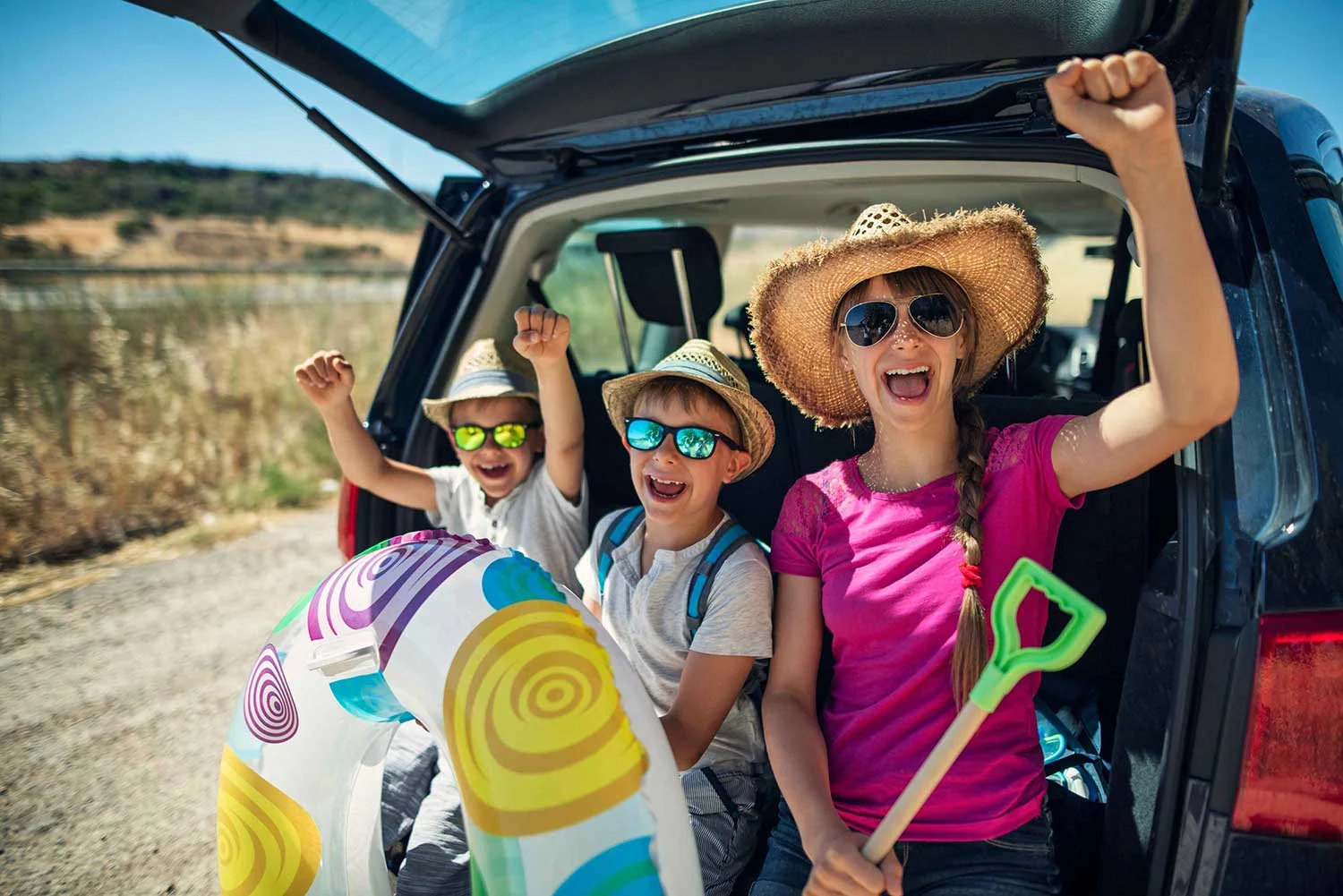 Glückliche Kinder mit Sonnenbrille und Badesachen sitzen in Kofferraum