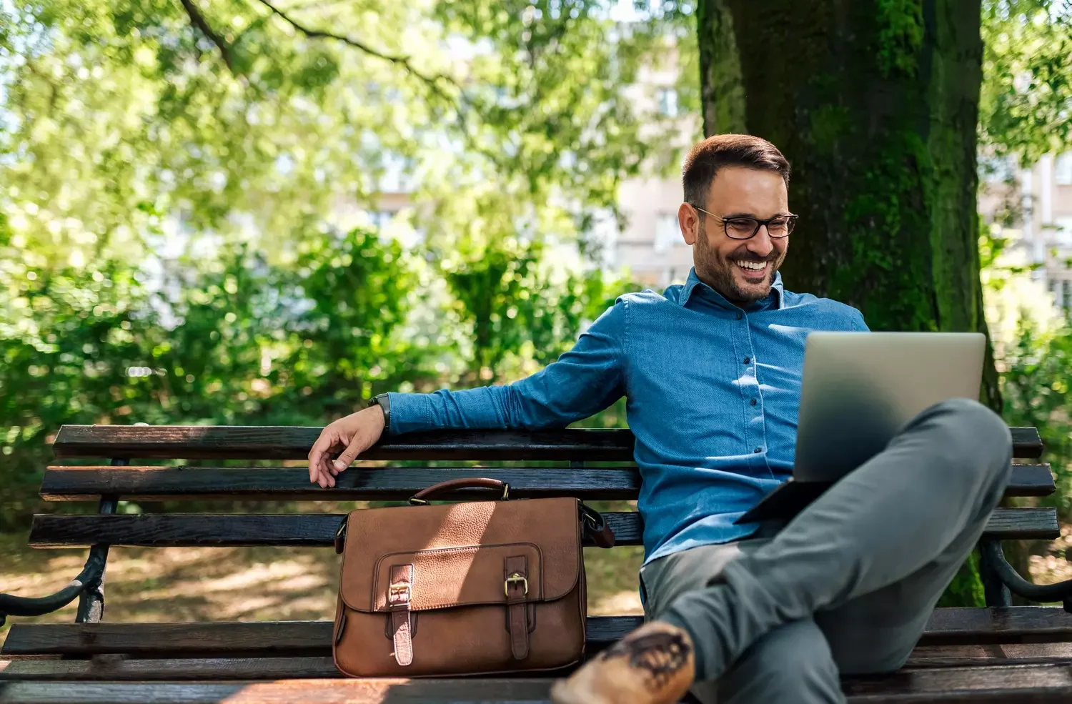 Netter junger Mann, der in einem Park mit Laptop sitzt.