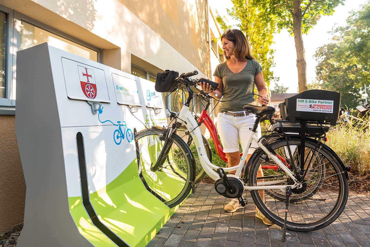 Frau stellt Ihr E-Bike in eine Ladestation. Frau stellt Ihr E-Bike in eine Ladestation.