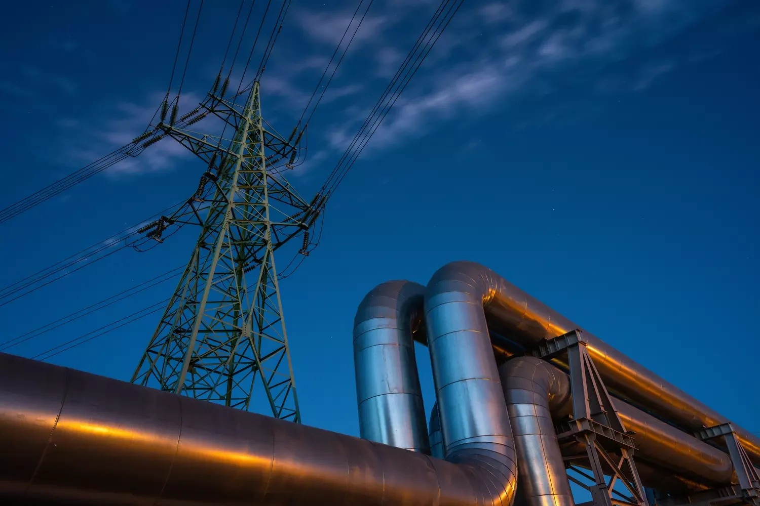 Rohrleitungen im Vordergrund und Strommast im Hintergrund