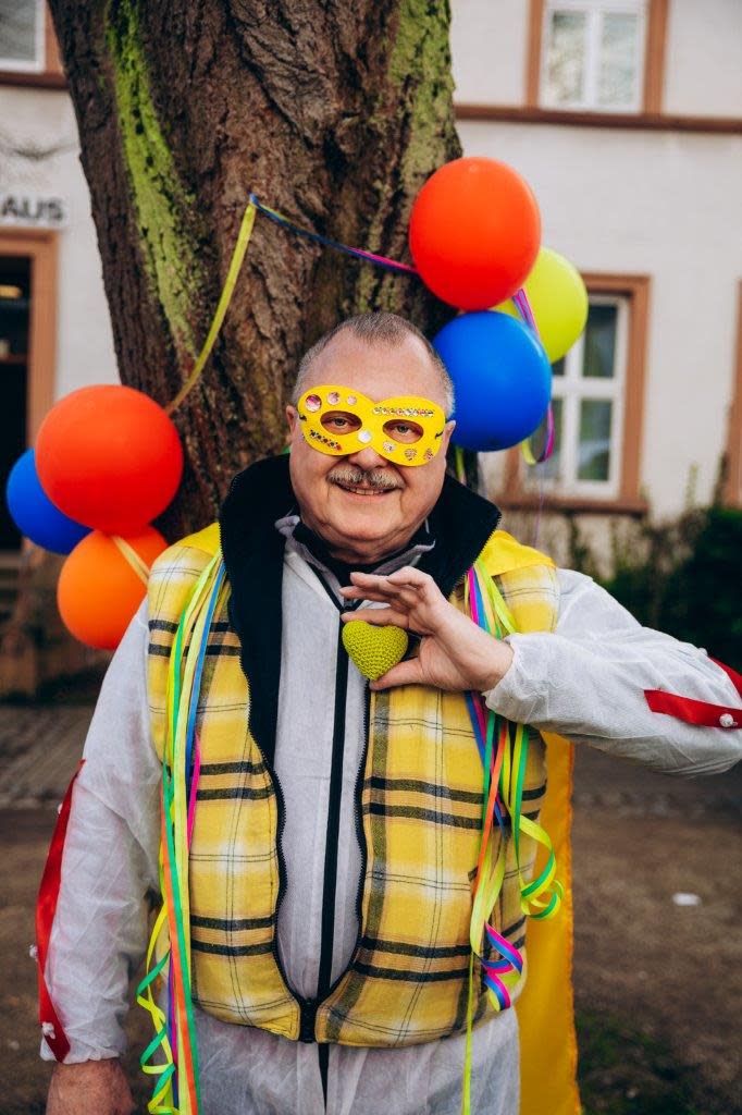 Hubertus Weber vom Heimatverein Horchheim steht verkleidet vor einem Baum. Der Baum ist mit roten, blauen und gelben Luftballons geschmückt.