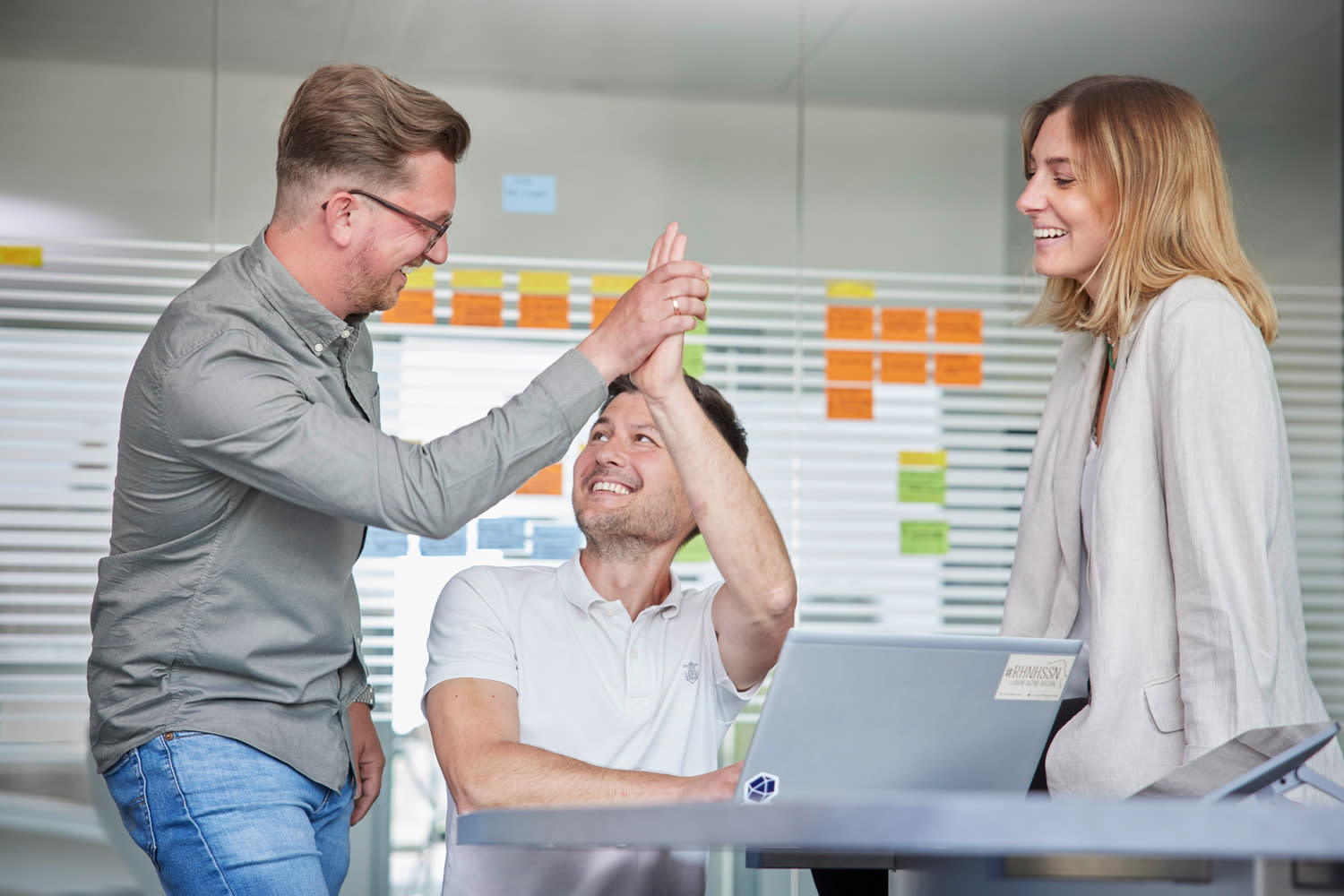 Drei Kollegen lachend im Meeting. Zwei Kollegen geben sich ein high five