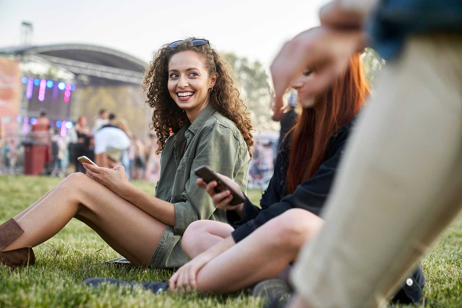 Frau sitzt mit Handy auf dem Gras auf einem Festival