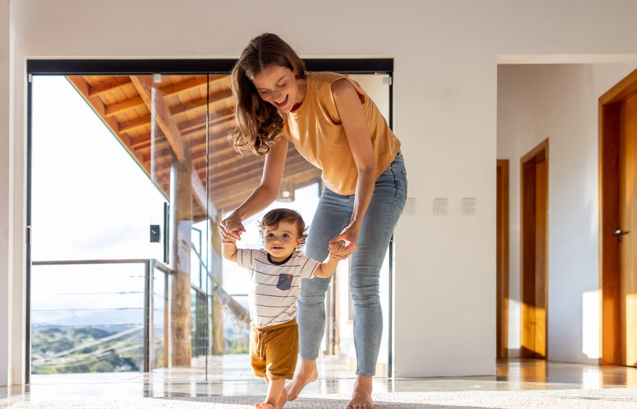 Kleinkind lernt zu Hause mit Hilfe seiner Mutter laufen.