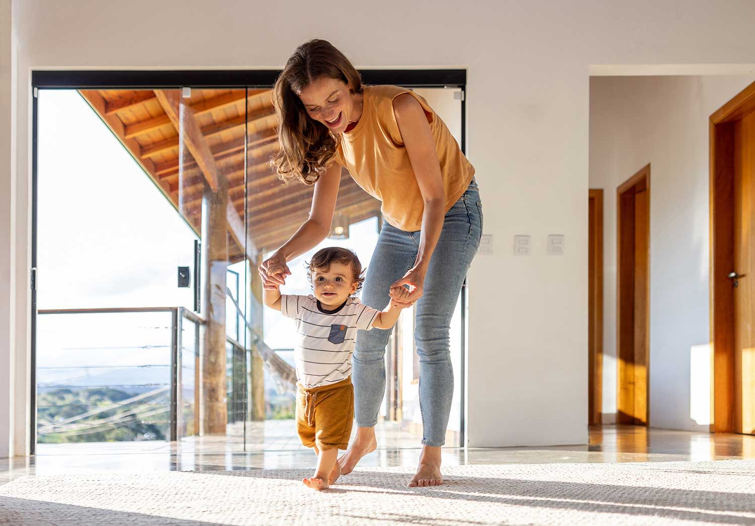 Kleinkind lernt zu Hause mit Hilfe seiner Mutter laufen