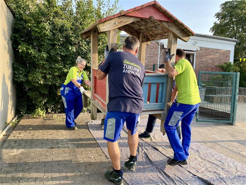 Starke Helferinnen und Helfer der EWR AG tragen ein Spielgerät zum streichen auf Malervlies.