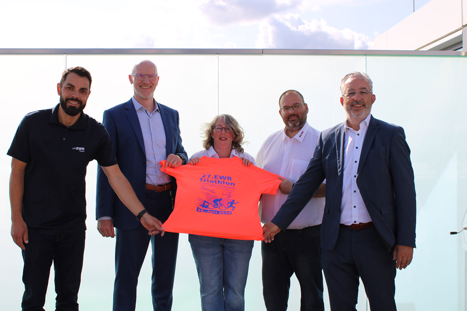 Titelbild EWR-Vorstände Stephan Wilhelm und Dieter Lagois, Pressesprecher Dominik Nagel und die Vertreter des DLRG Lampertheim halten das diesjährige Trikot des EWR-Triathlons in der Hand