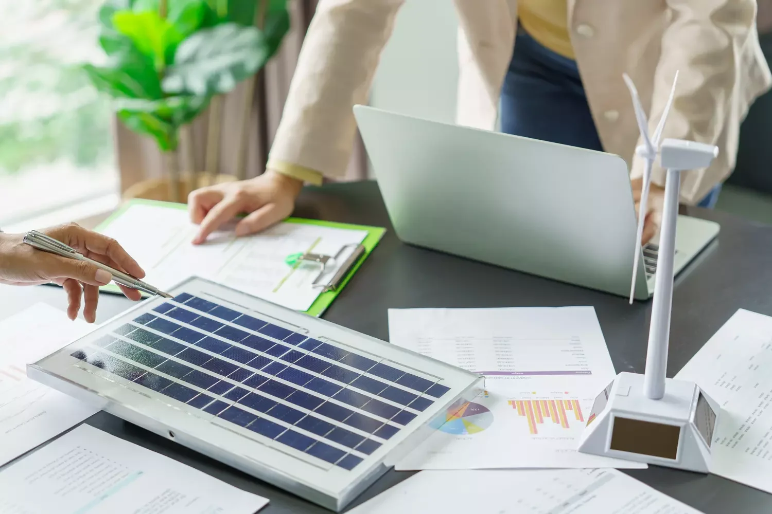 Schreibtisch im Büro mit Photovoltaik, Windrad, Laptop und Personen