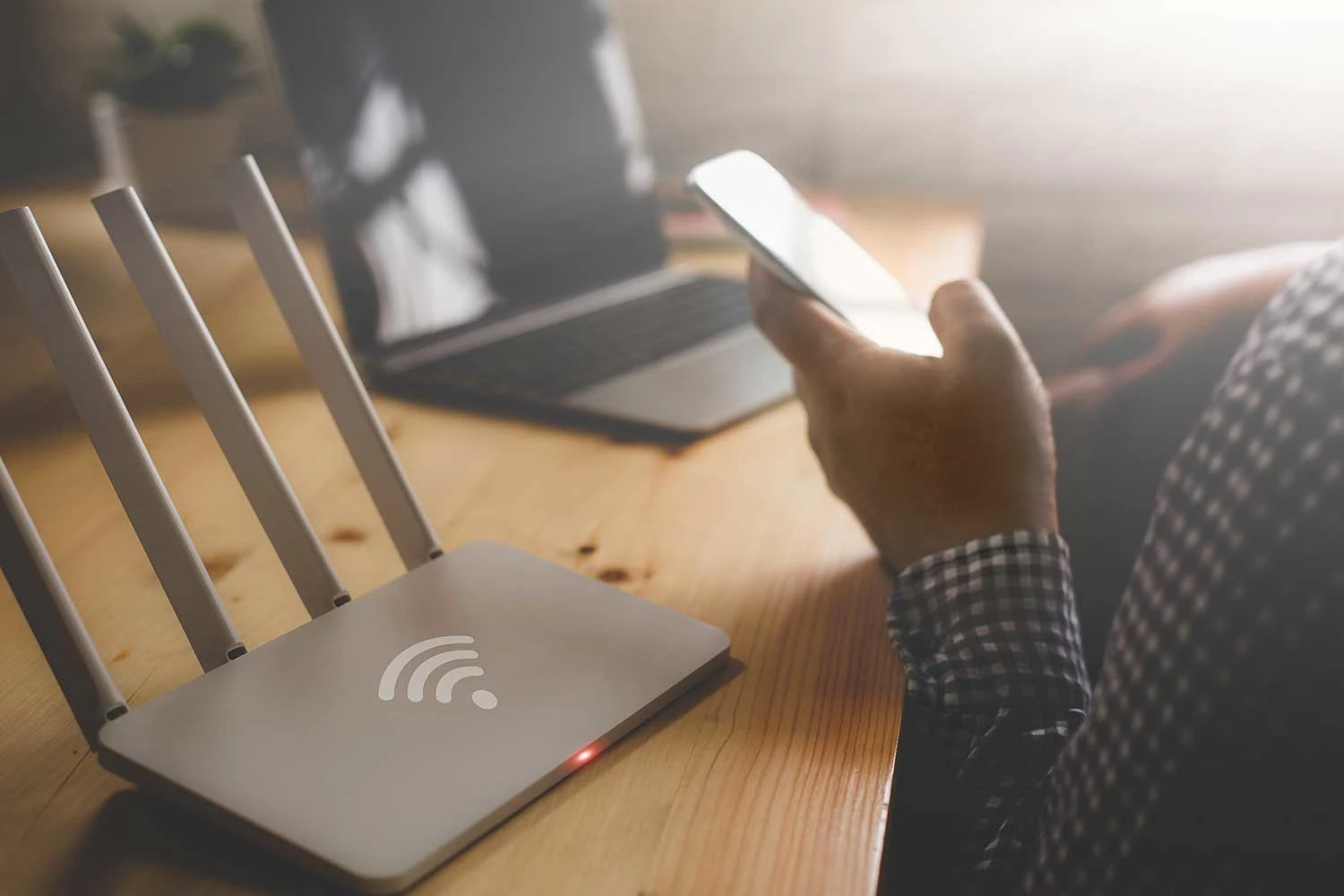 Eine Männerhand hält Smartphone und Laptop und Router stehen auf dem Tisch