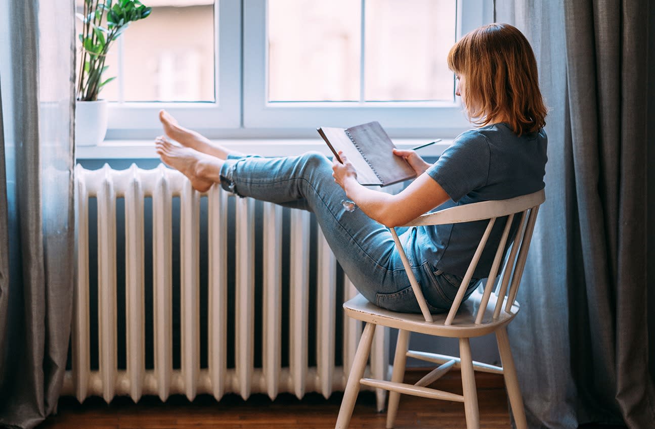 Frau sitzt barfuß an einer Heizung und liest ein Buch