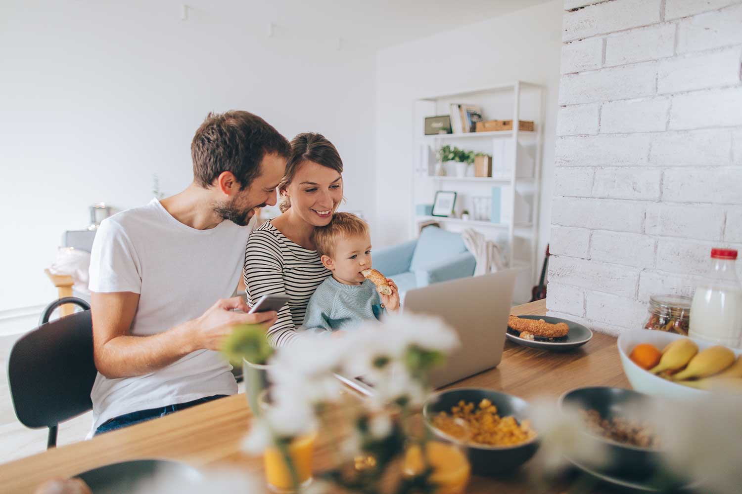 Junge Familie sitzt am Laptop am Frühstückstisch