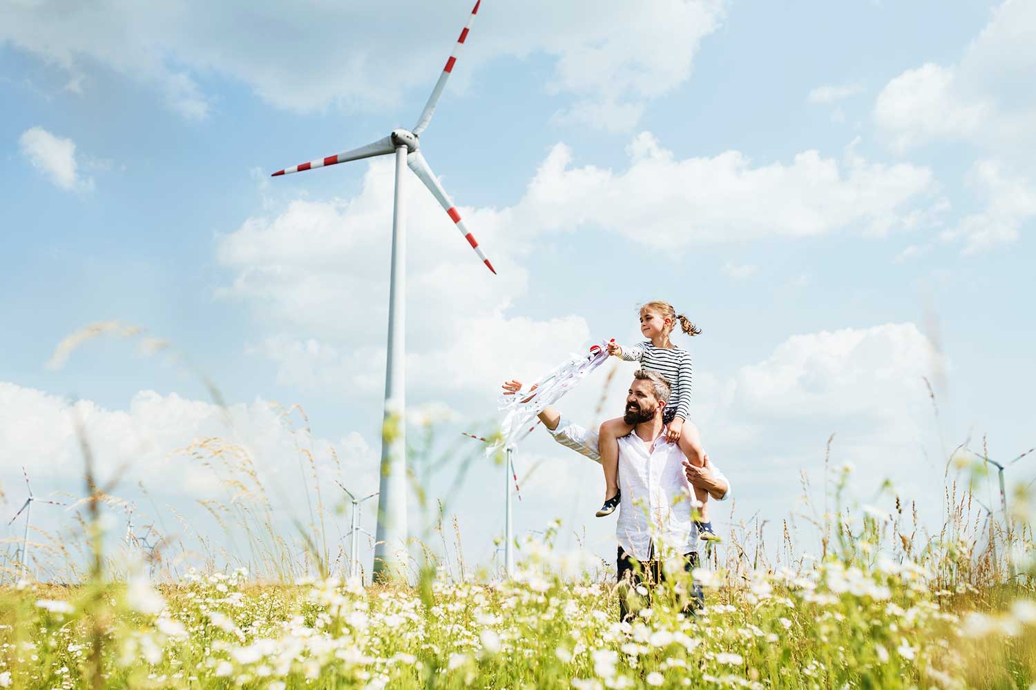 Vater mit kleiner Tochter auf der Schulter zu Fuß auf dem Feld im Windpark