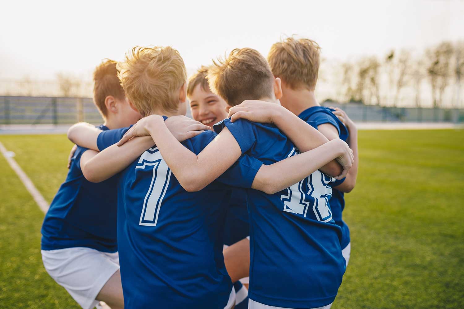 Kinder-Fußballteam hüpft im Kreis auf dem Sportplatz