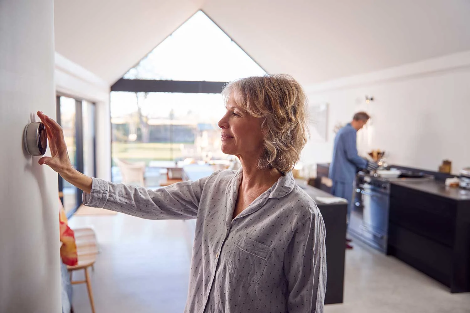Eine Frau stellt an der Wand über einen montierten Regler das Thermostat der Zentralheizung im Haus ein